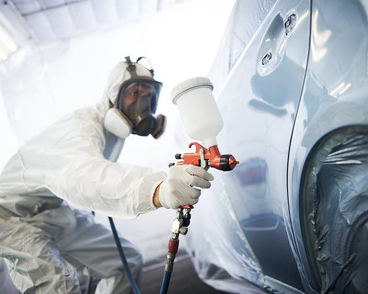 Technician spray-painting a car panel in the paint booth